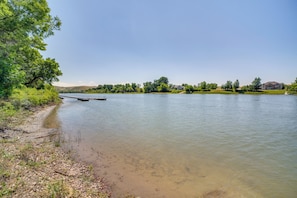 A riverbank with a dock, trees, and a house in the background.