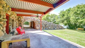 A covered outdoor area with a stone wall, a wooden bench, and a red chair. - Cozy Great Falls Studio on the Missouri River! (Great Falls)