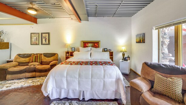 A bedroom with a large bed, a sofa, a chair, and a nightstand with lamps. - Cozy Great Falls Studio on the Missouri River! (Great Falls)