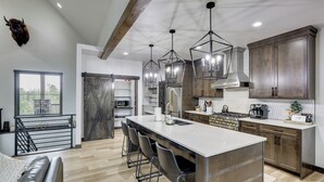 A modern kitchen with a central island, bar stools, stainless steel appliances, and a large window. - Luxurious Lead Vacation Rental w/ Private Hot Tub! (Lead)
