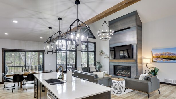 A modern kitchen with a large island, a dining area with a table and chairs, a living room with a sofa and fireplace, and large windows with a view of trees. - Luxurious Lead Vacation Rental w/ Private Hot Tub! (Lead)