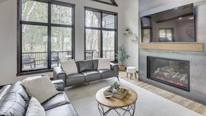 A modern living room with a fireplace, large windows, a leather sofa, and a round coffee table. - Luxurious Lead Vacation Rental w/ Private Hot Tub! (Lead)