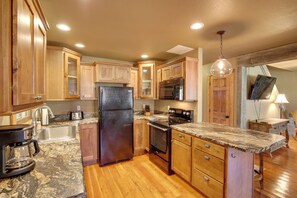 A kitchen with wooden cabinets, a granite countertop, stainless steel appliances, and a hanging light fixture. - Cozy Lead Cabin w/ Deck < 1 Mi to Ski Slopes! (Lead)