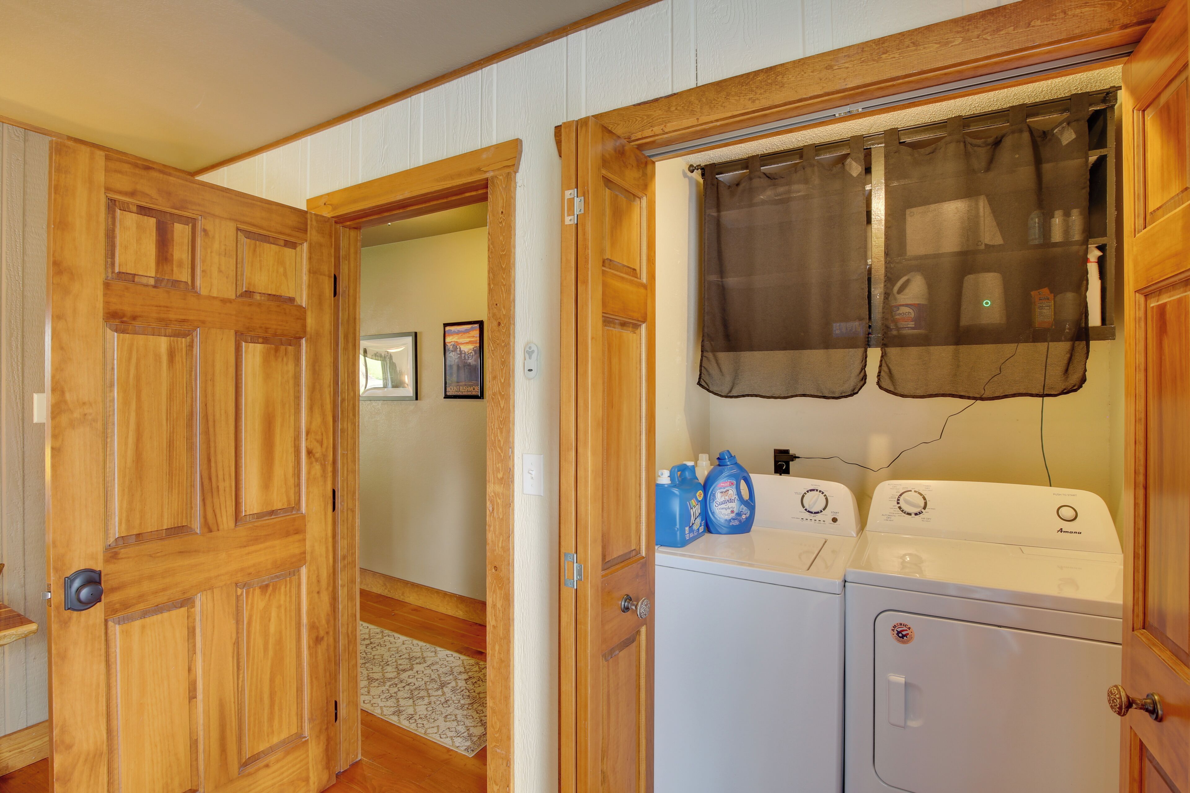 Un área de lavandería con dos lavadoras, puertas de madera y un ventanal con cortina.