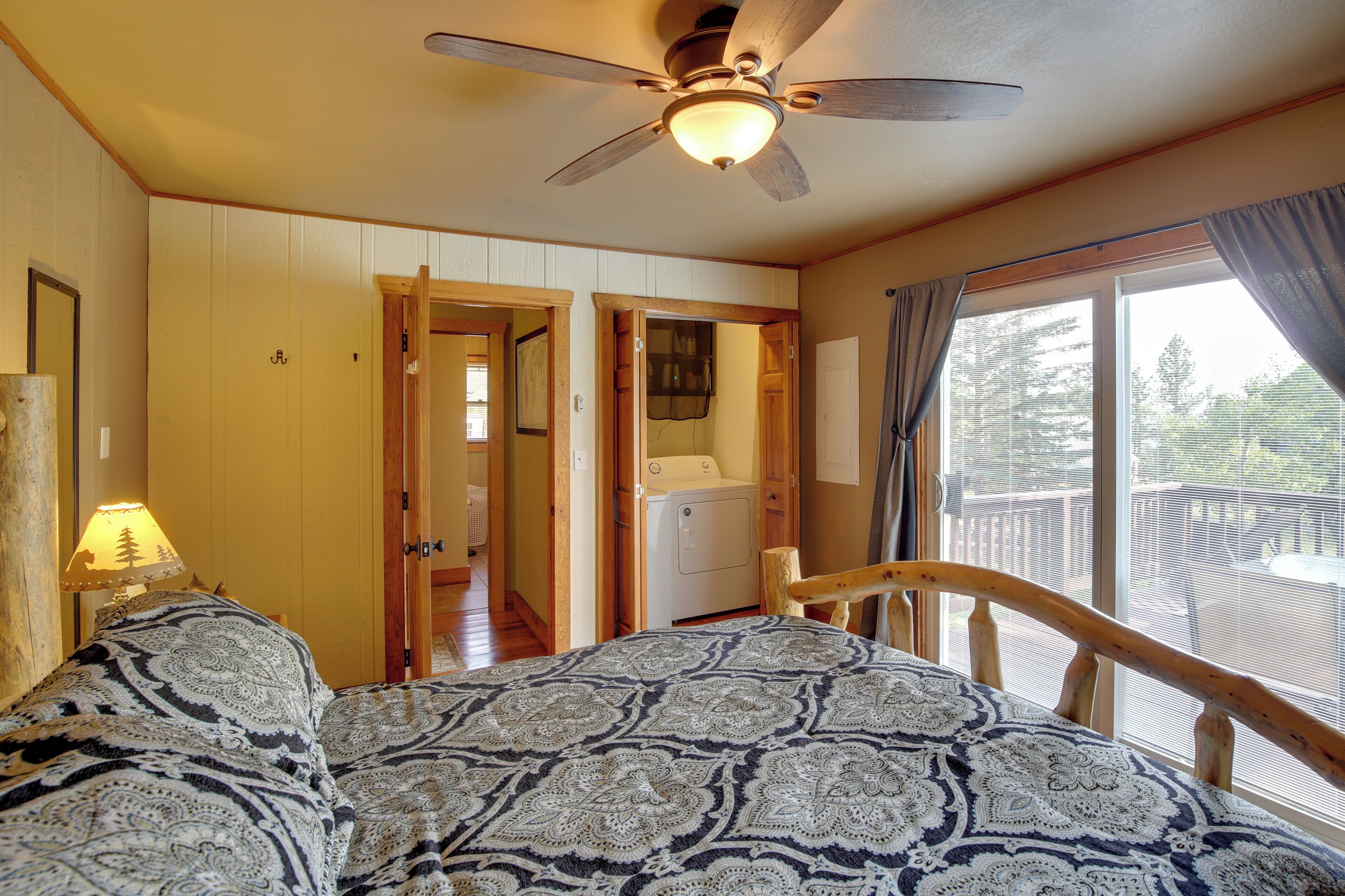 Une chambre à coucher avec un lit, un ventilateur de plafond, une fenêtre avec des rideaux et une vue sur l’extérieur.