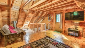 A cozy attic bedroom with wooden beams, a sofa, a TV, and a bookshelf. - Charming Wellesley Island Cabin Near State Parks (Wellesley Island)