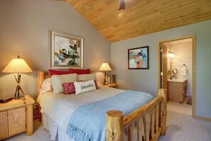 A bedroom with a wooden headboard, a bed with multiple pillows, two bedside lamps, a framed artwork above the bed, and a bathroom visible through an open door. - Lakefront Brainerd Cabin w/ Fireplace! (Brainerd)