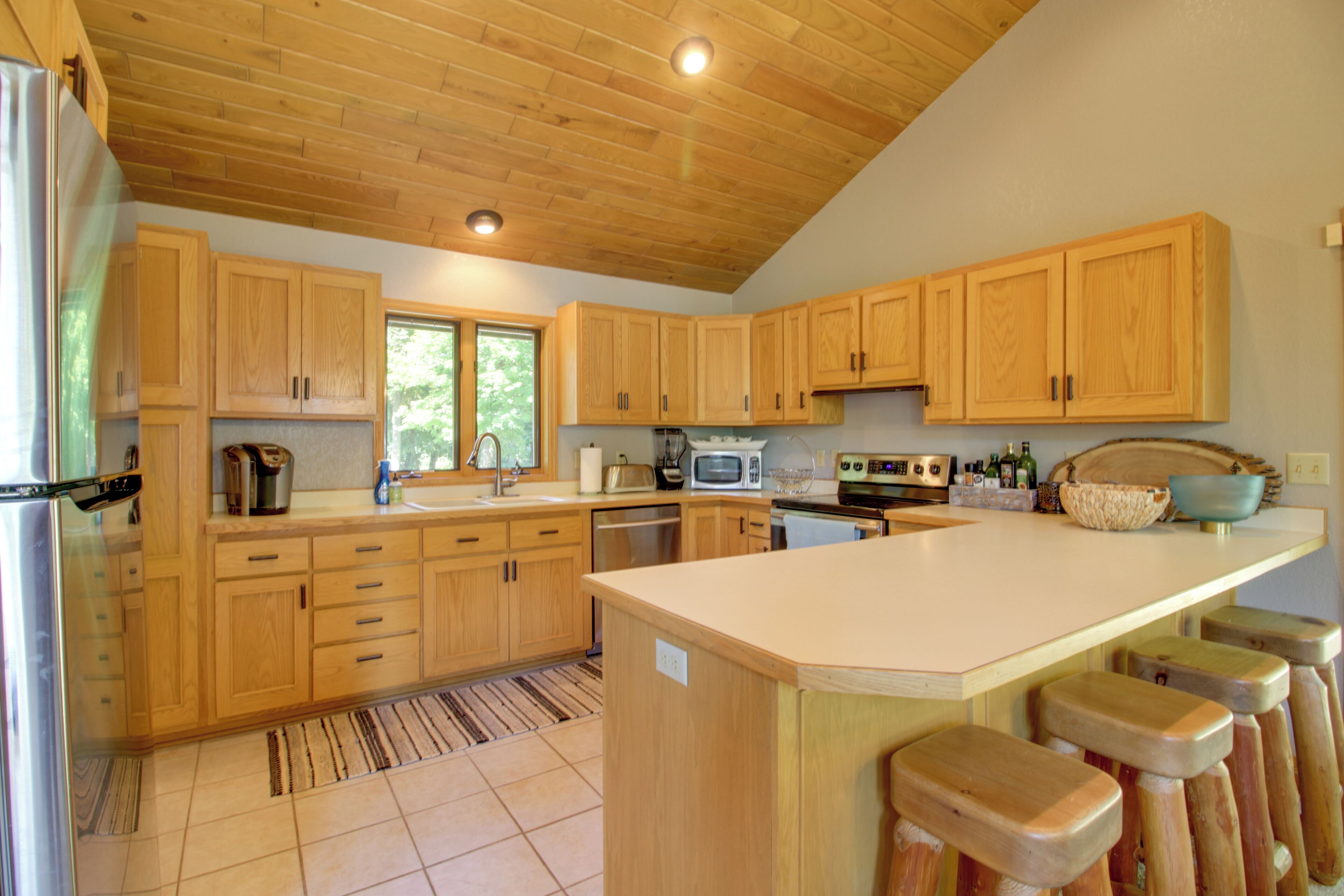 A spacious kitchen with wooden cabinets, a central island with stools, a refrigerator, a microwave, and a dishwasher.