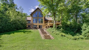 A large wooden house with a prominent staircase leading to a deck, surrounded by lush greenery. - Lakefront Brainerd Cabin w/ Fireplace! (Brainerd)