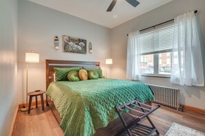 Quarto com cama, radiador, janela com cortinas, luminária de chão e um quadro na parede.