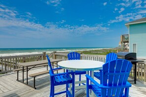 A wooden deck with a round table and blue chairs overlooking the ocean.