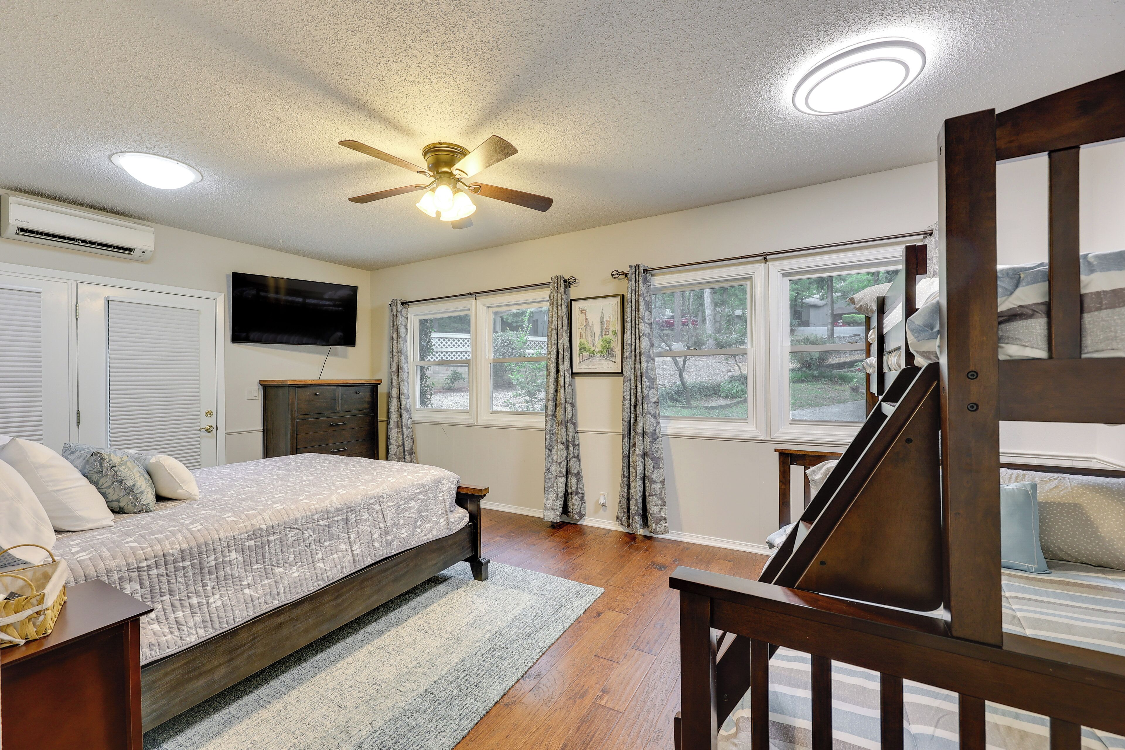 A bedroom with a bed, a ceiling fan, a TV, and a window with curtains.
