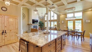 A spacious kitchen with a large island, wooden cabinets, and a stone fireplace. - Hot Tub + Golf Course Views: Luxe Sturgis Home! (Sturgis)
