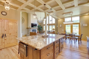A spacious kitchen with a large island, wooden cabinets, and a stone fireplace. - Hot Tub + Golf Course Views: Luxe Sturgis Home! (Sturgis)