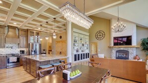 A spacious kitchen with a central island, wooden cabinets, and a stone fireplace. - Hot Tub + Golf Course Views: Luxe Sturgis Home! (Sturgis)