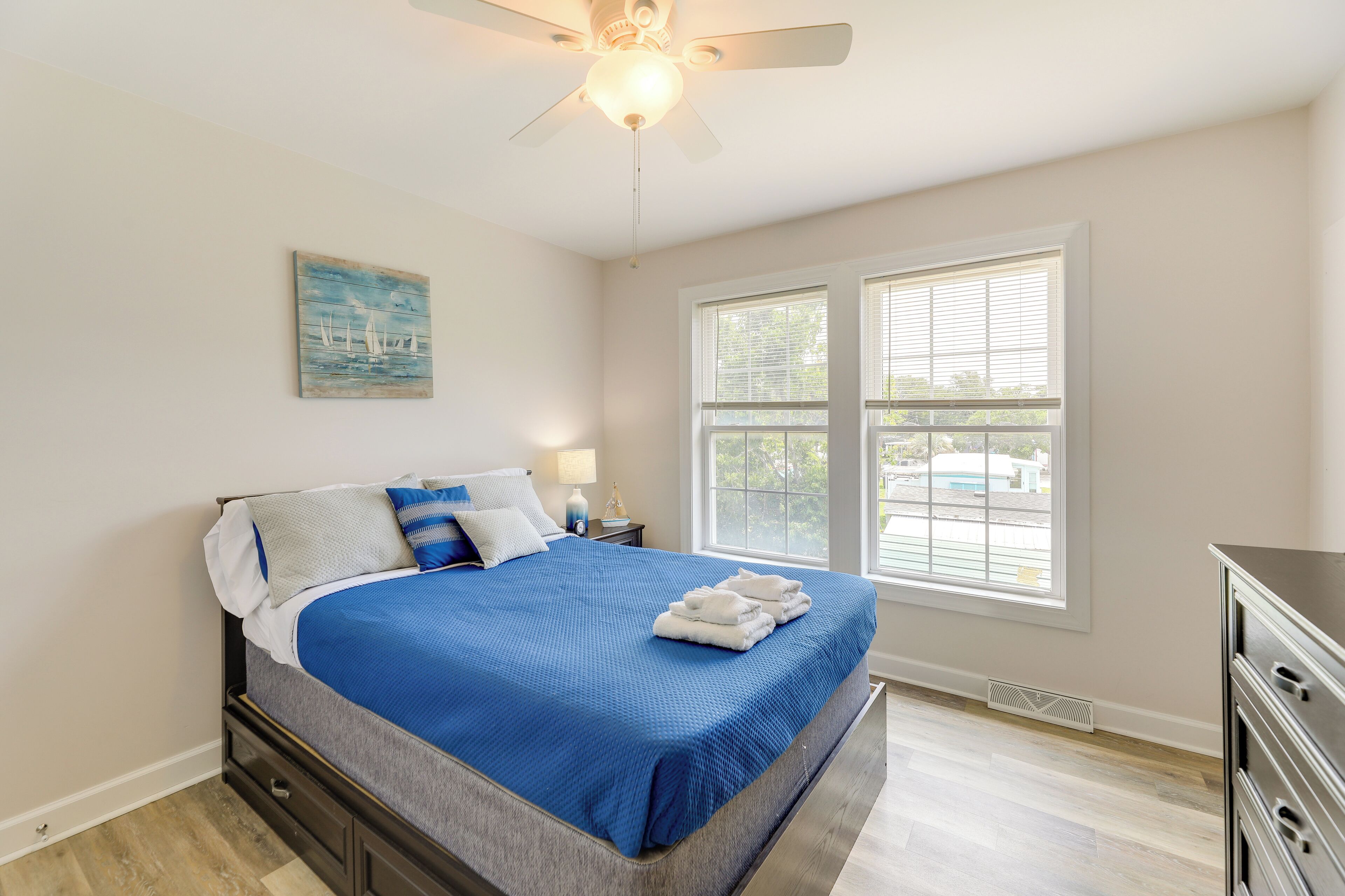A bedroom with a bed, a ceiling fan, a window, and a dresser.