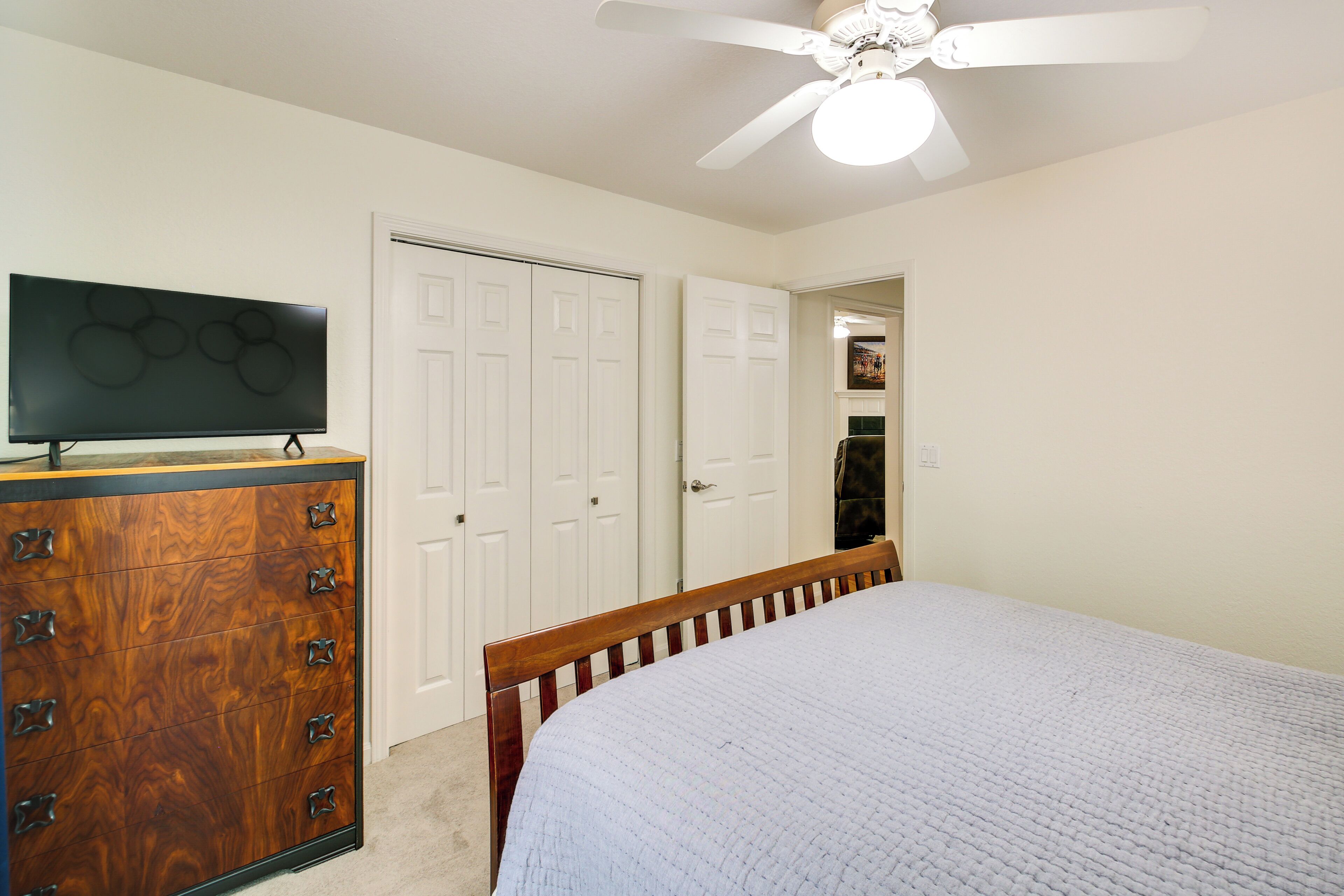 A bedroom with a bed, a dresser, a television, and a ceiling fan.