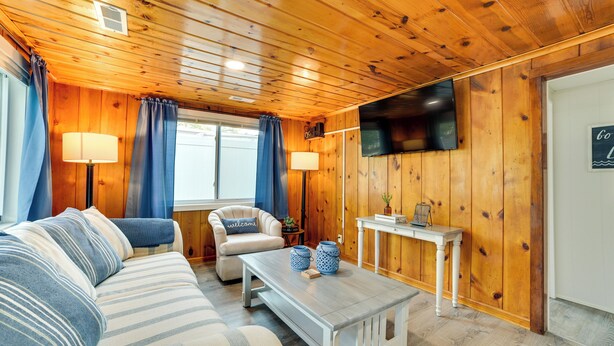 Ein gemütliches Zimmer mit Holzwänden, einer Couch, einem Sessel, einem Couchtisch und einem an der Wand befestigten Fernseher.