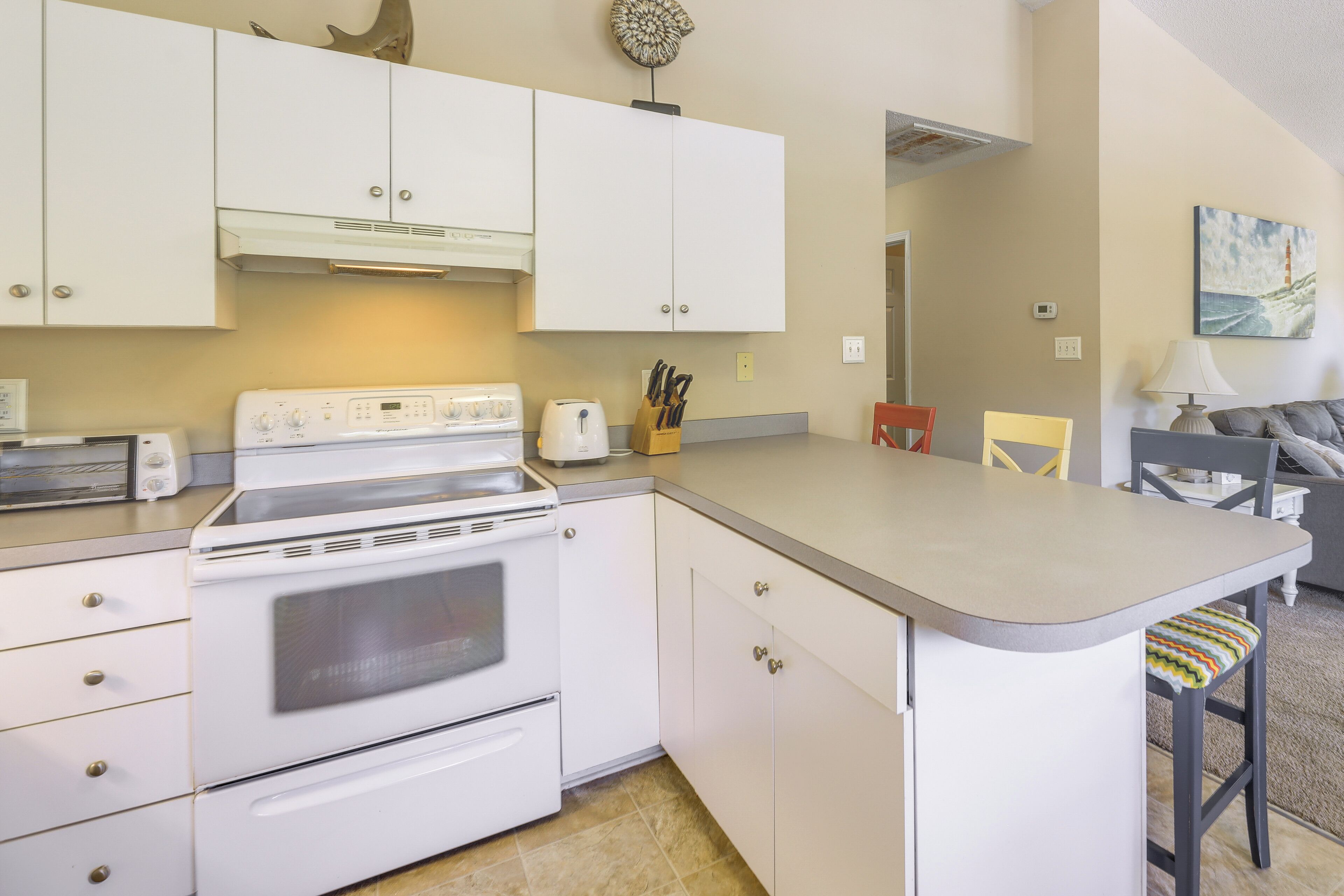 A compact kitchen with white cabinets, a built-in oven, and a small dining area with a chair and table.