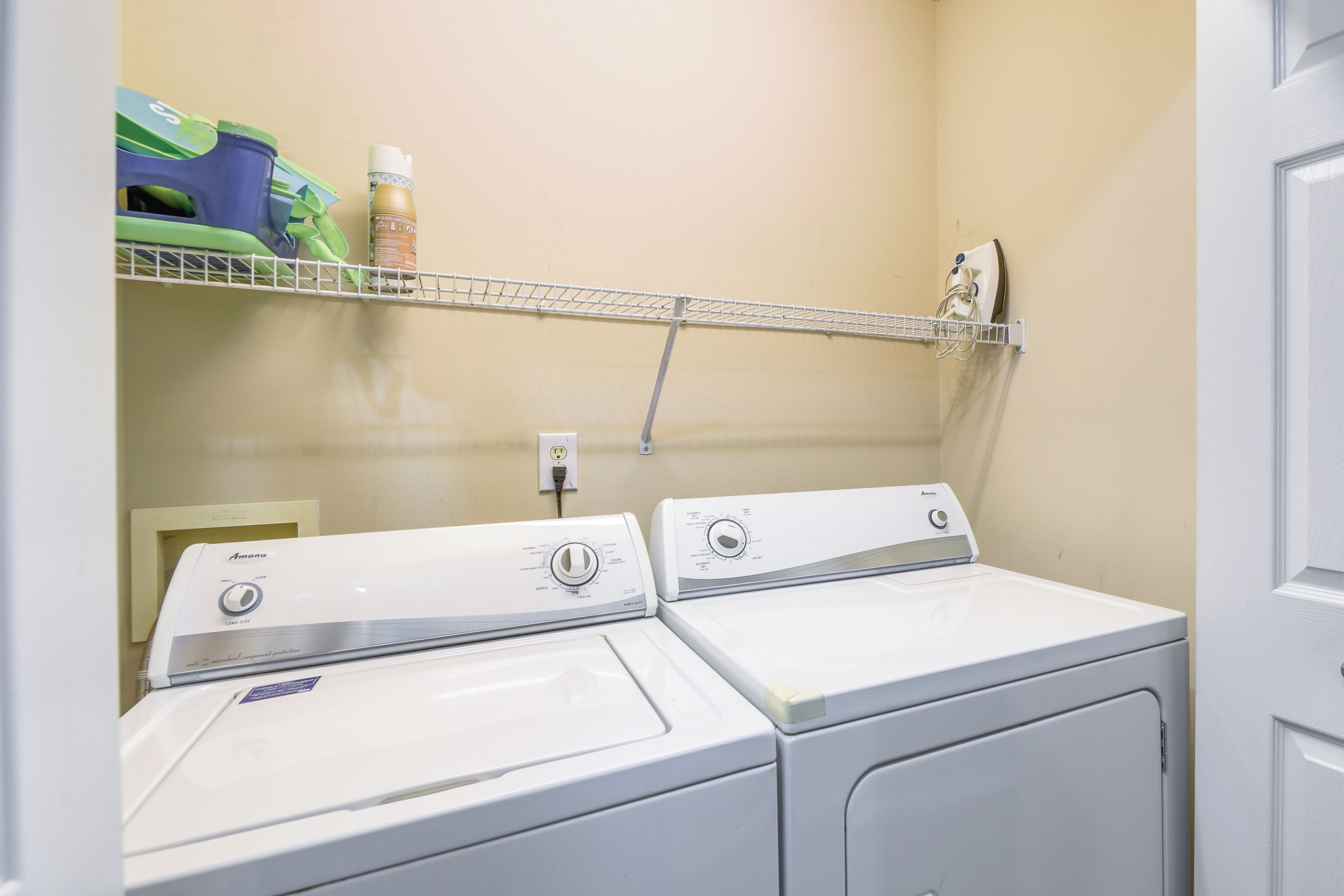 A laundry area with two white front-loading washers and a shelf above holding cleaning supplies.