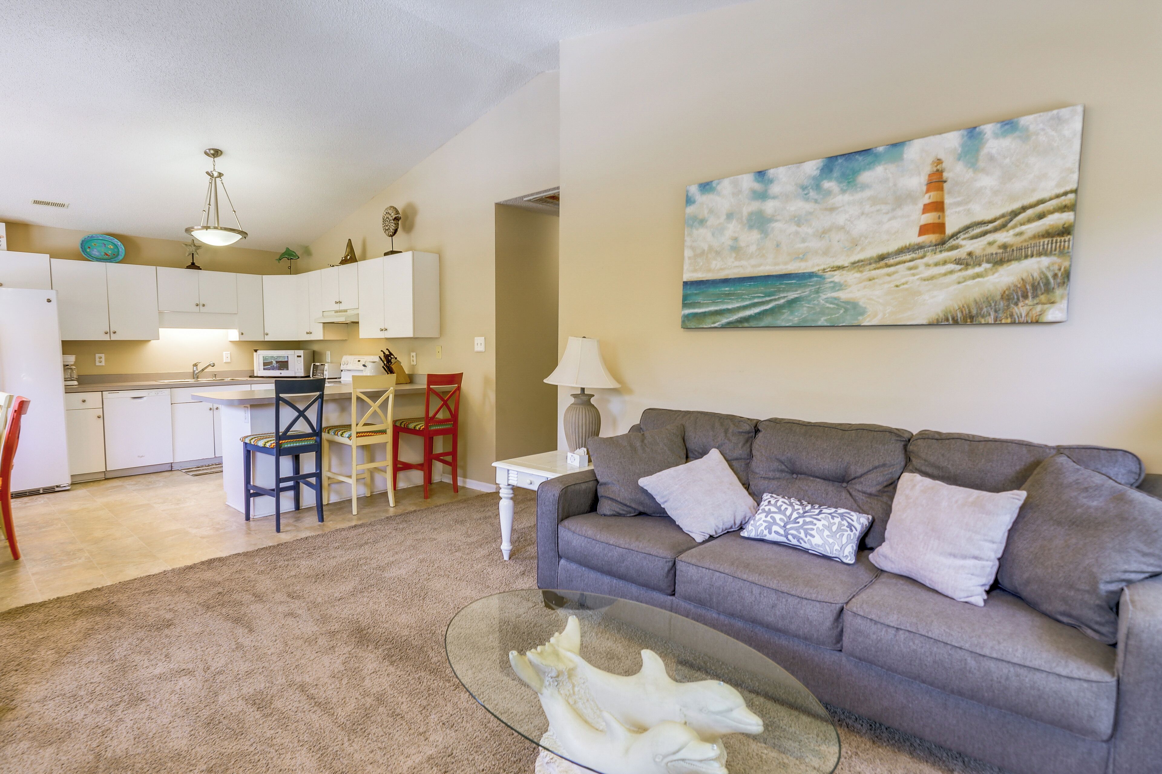 A living room with a grey sofa, a glass coffee table, and a painting of a lighthouse.