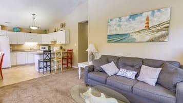 A living room with a grey sofa, a glass coffee table, and a painting of a lighthouse.