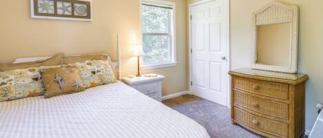 A bedroom with a bed, a nightstand, a dresser, a window, and a door.