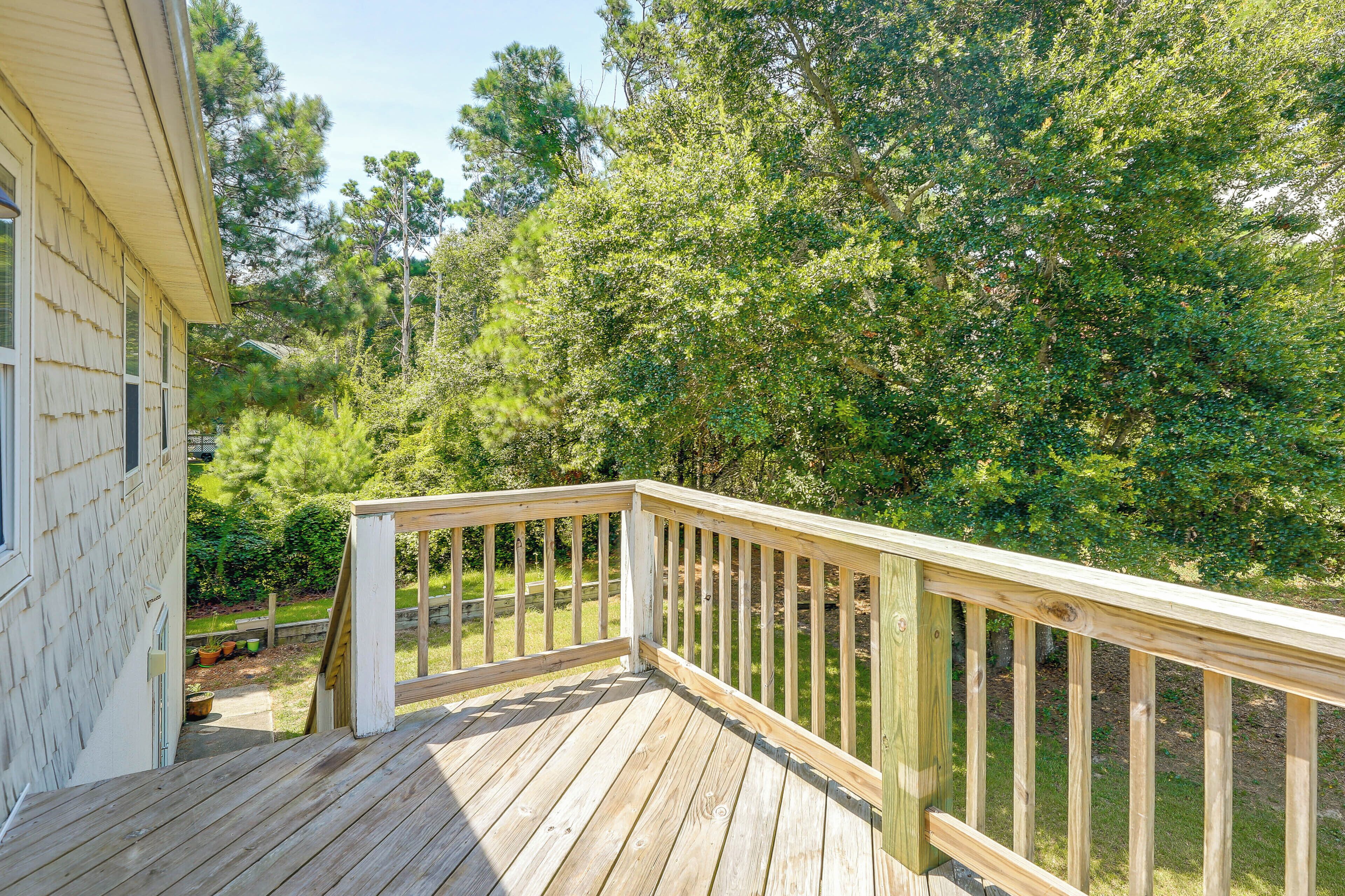 A wooden deck with a railing, surrounded by lush greenery and trees.