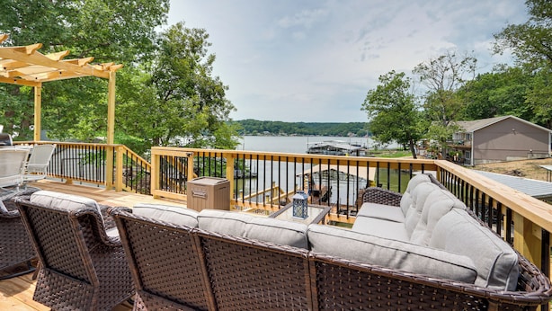 Una terraza con mobiliario de mimbre, una pérgola y vistas a un lago y barcos.