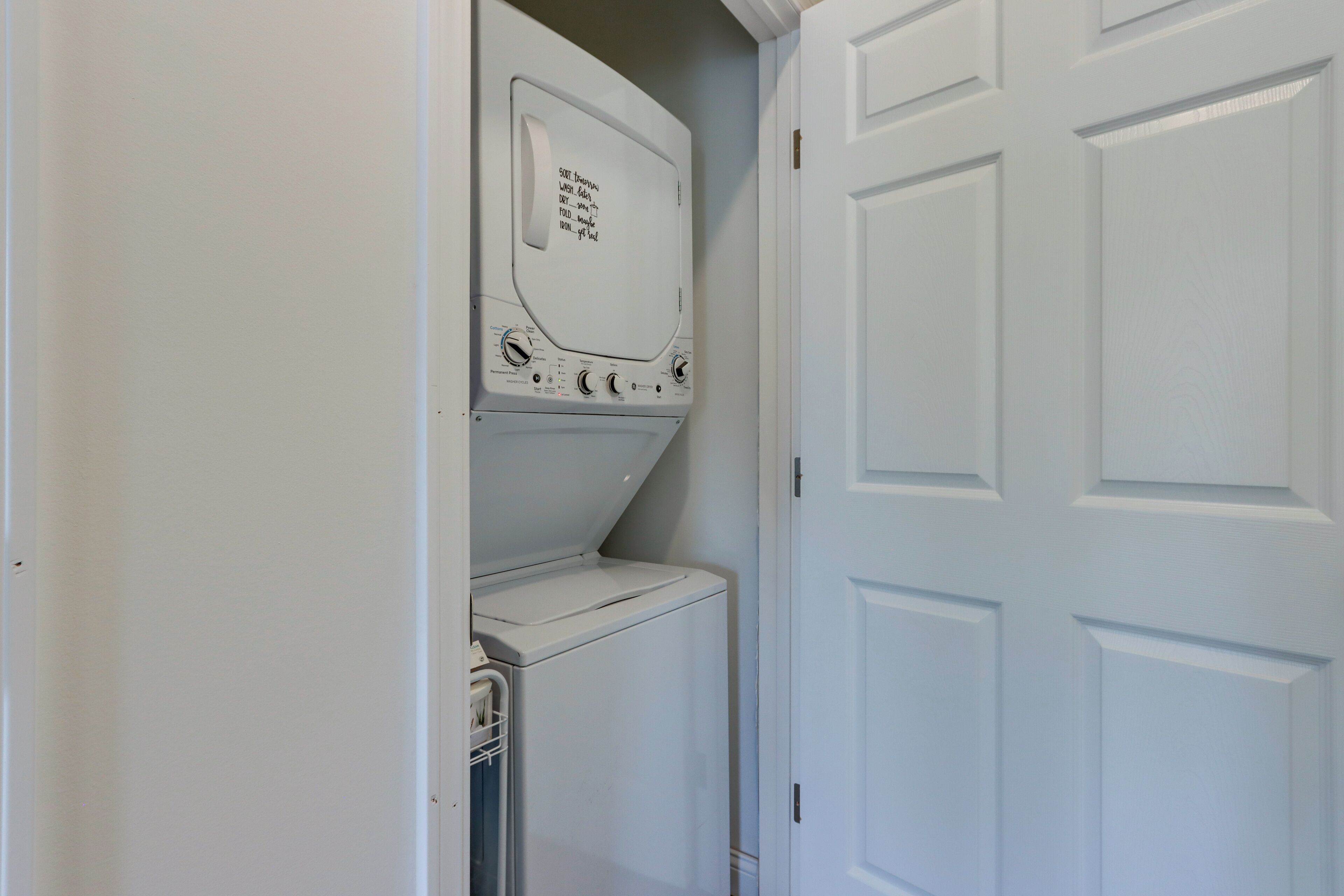 A laundry room with a front-loading washer and dryer, a door, and a wall-mounted control panel.