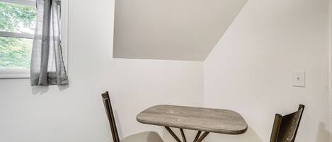 A small dining area with a table and two chairs, a window with curtains, and a white wall.
