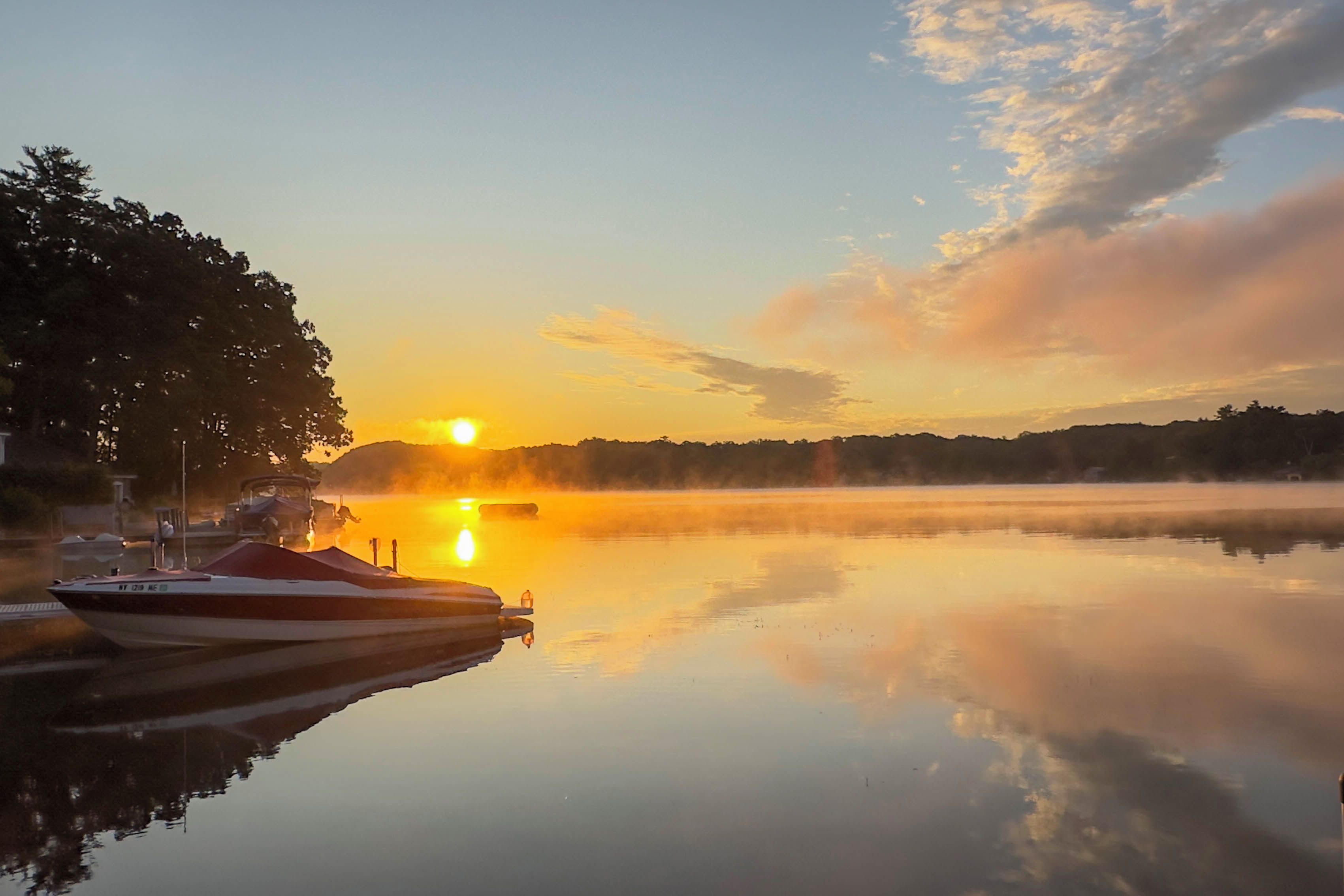 Un lago tranquillo all'alba, con barche ormeggiate a sinistra e un cielo sereno.
