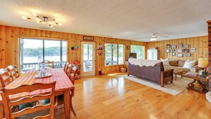 A spacious room with wooden walls and a large dining table. There is a sofa and a small table with a lamp. - Lakefront Queensbury Home: Kayaks + Boat Dock (Lake George)