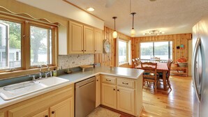 A kitchen with wooden cabinets, a sink, and a dining area with a table and chairs. - Lakefront Queensbury Home: Kayaks + Boat Dock (Lake George)