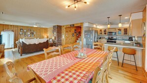 A spacious kitchen with wooden cabinets, a dining area with a checkered tablecloth, and a cozy living room with a sofa. - Lakefront Queensbury Home: Kayaks + Boat Dock (Lake George)