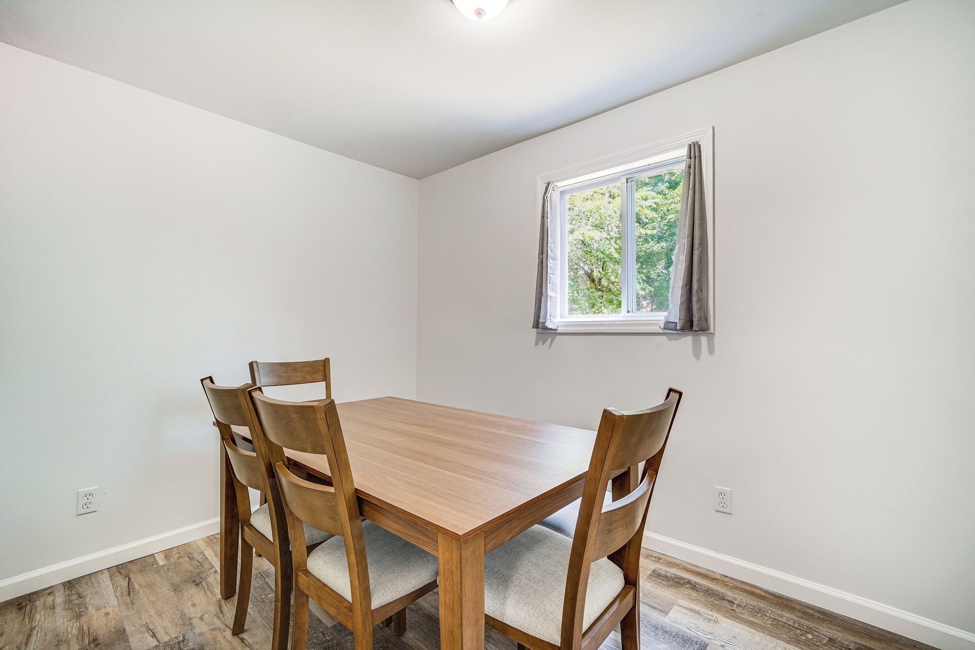 Un coin repas avec une table en bois et quatre chaises, une fenêtre avec des rideaux et un mur blanc.
