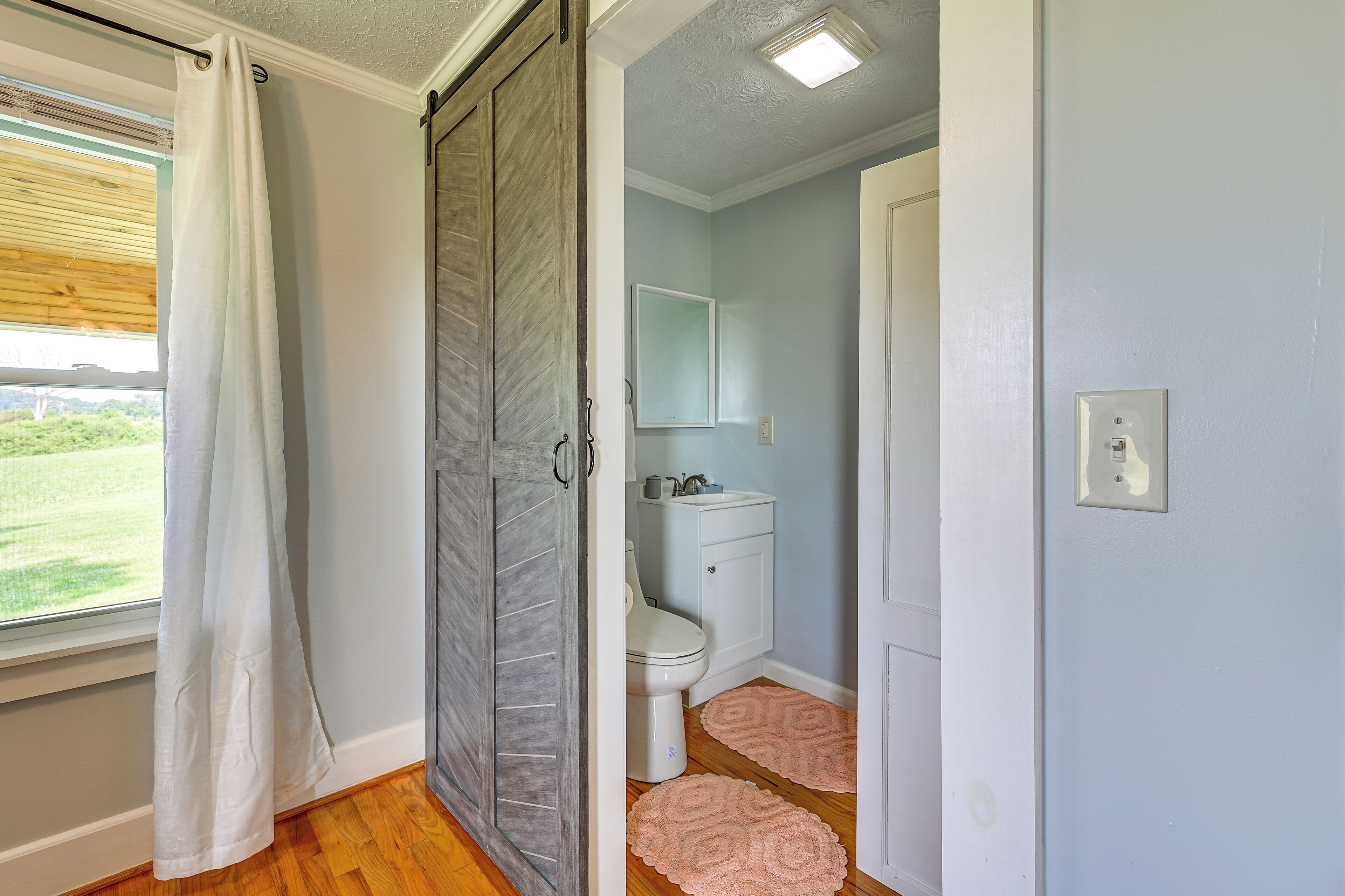 A bathroom with a toilet, sink, mirror, and a window with a curtain.