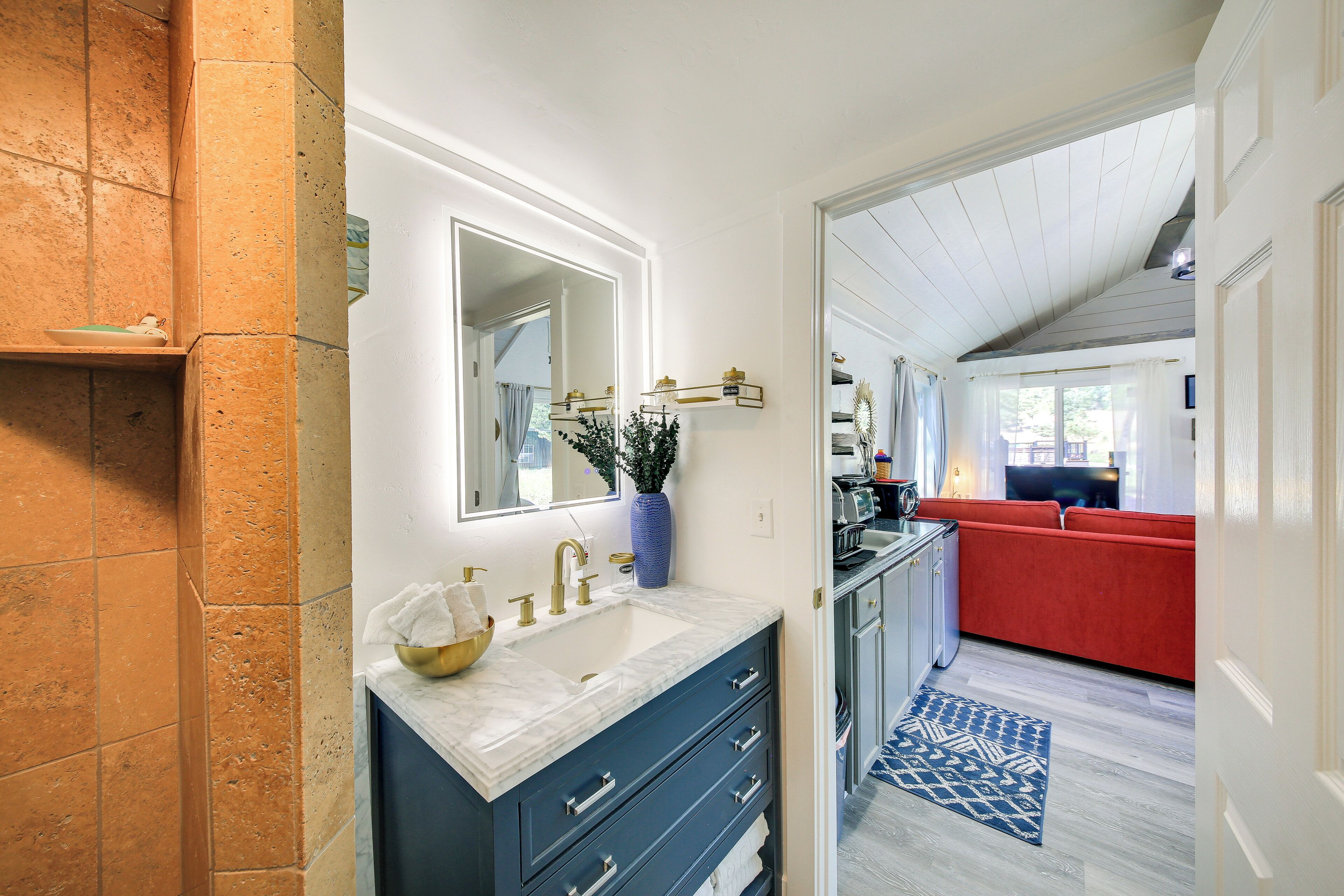 A bathroom with a marble sink, a mirror, and a vase with a plant.