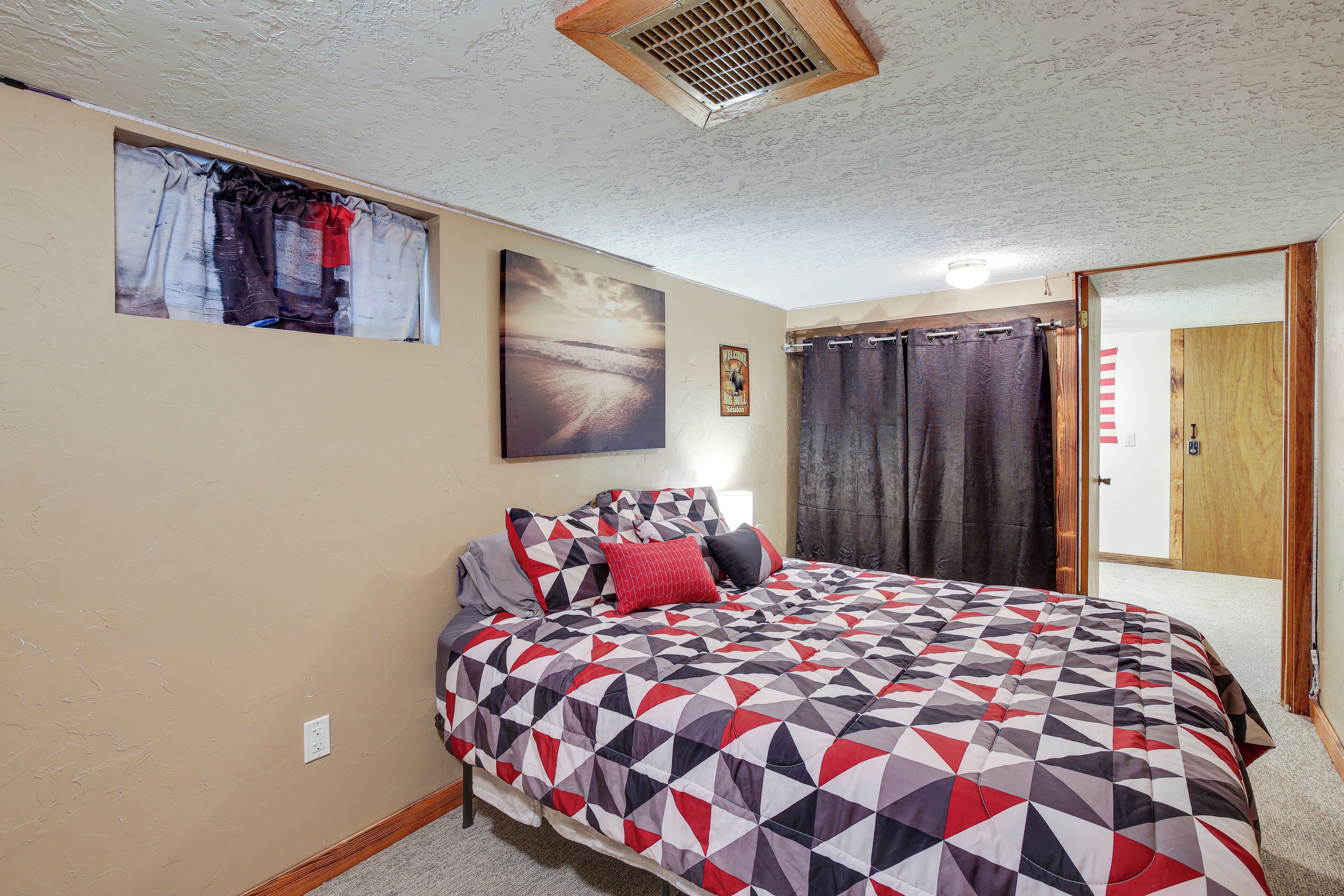 A bedroom with a bed, a window with curtains, a door, and a wall-mounted picture.