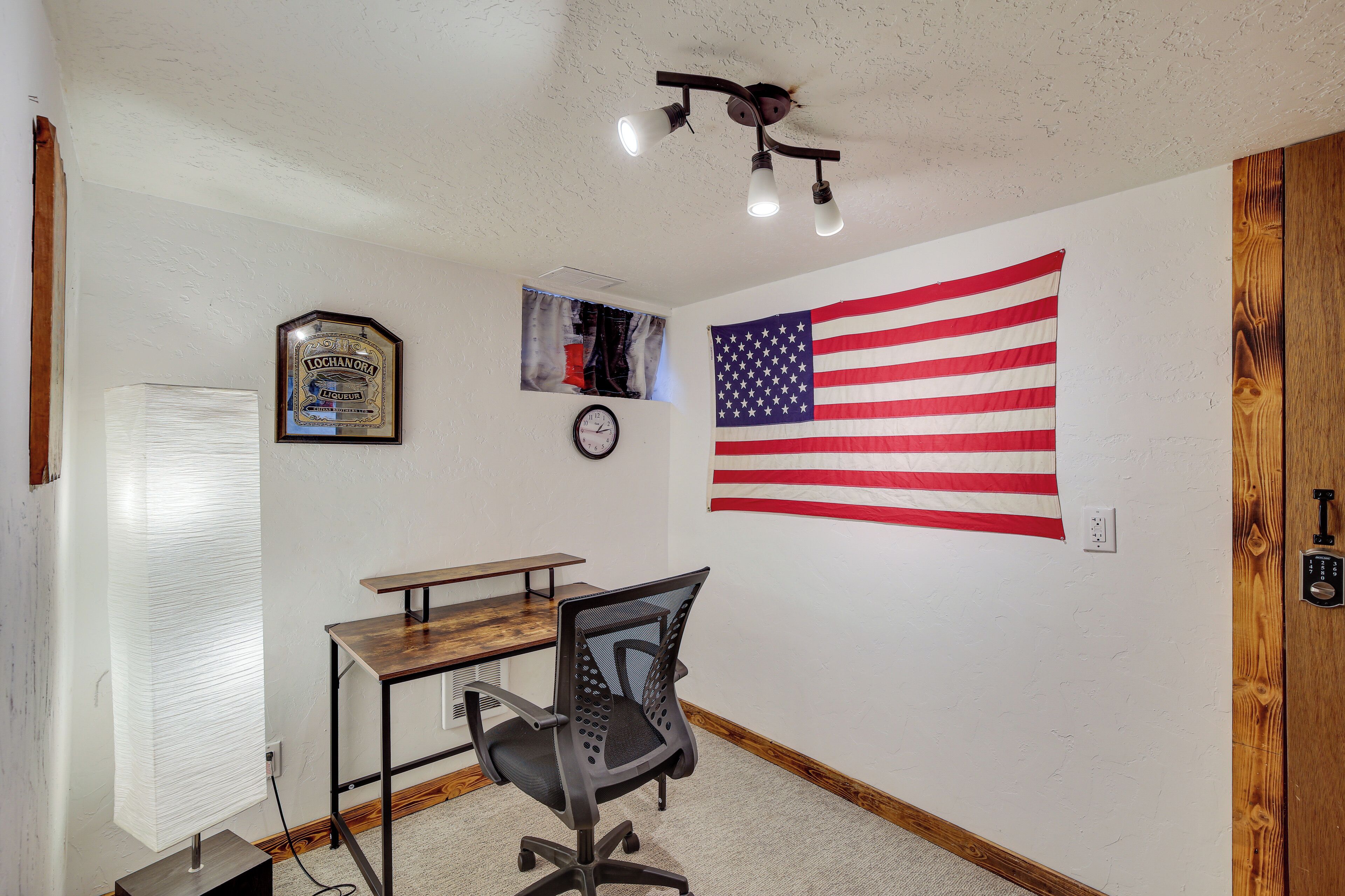 A room with a desk, chair, American flag, clock, and a framed certificate on the wall.