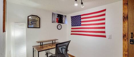A room with a desk, chair, American flag, clock, and a framed certificate on the wall.