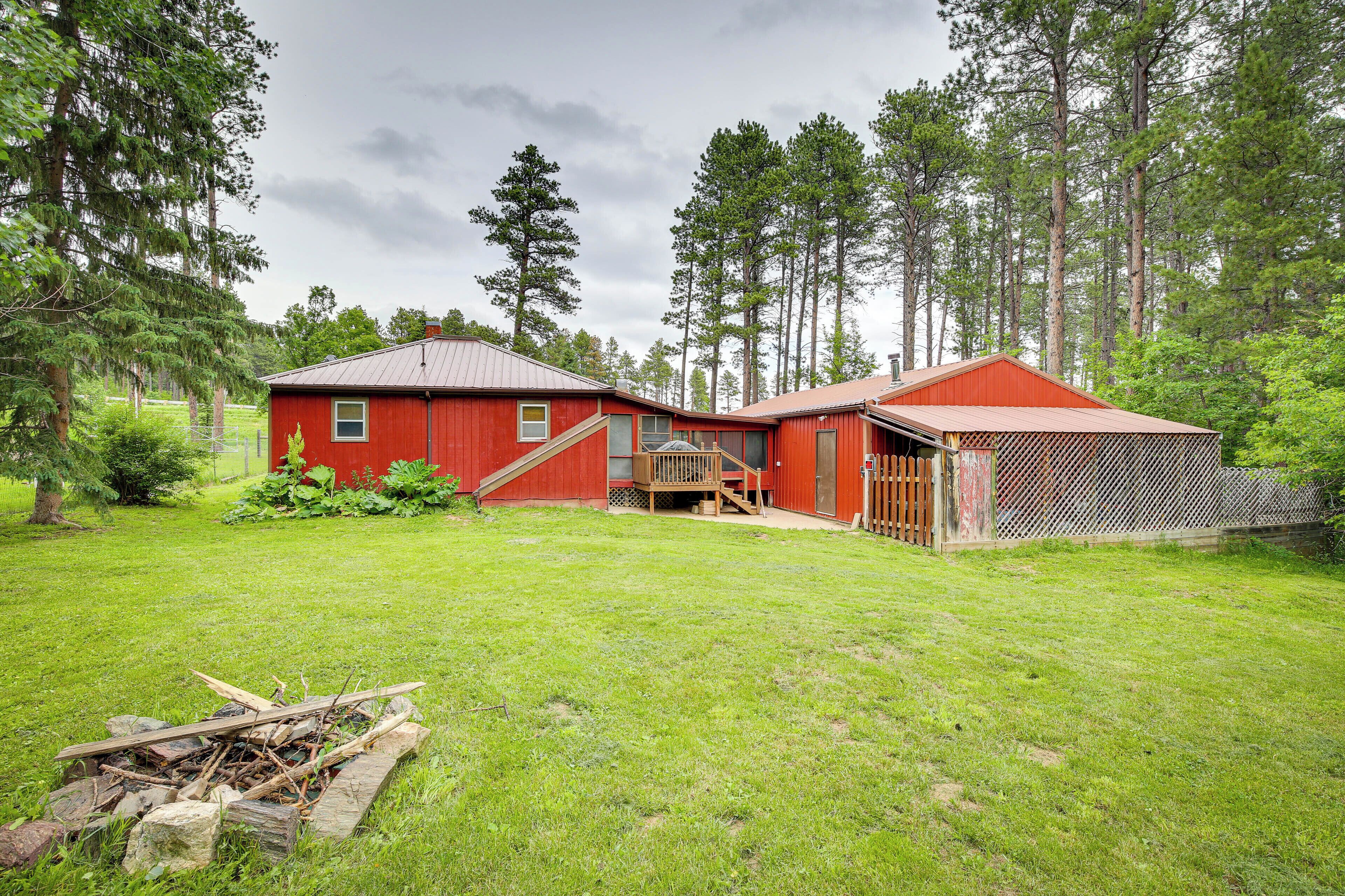 A red wooden cabin with a metal roof, a wooden deck, and a fenced yard.