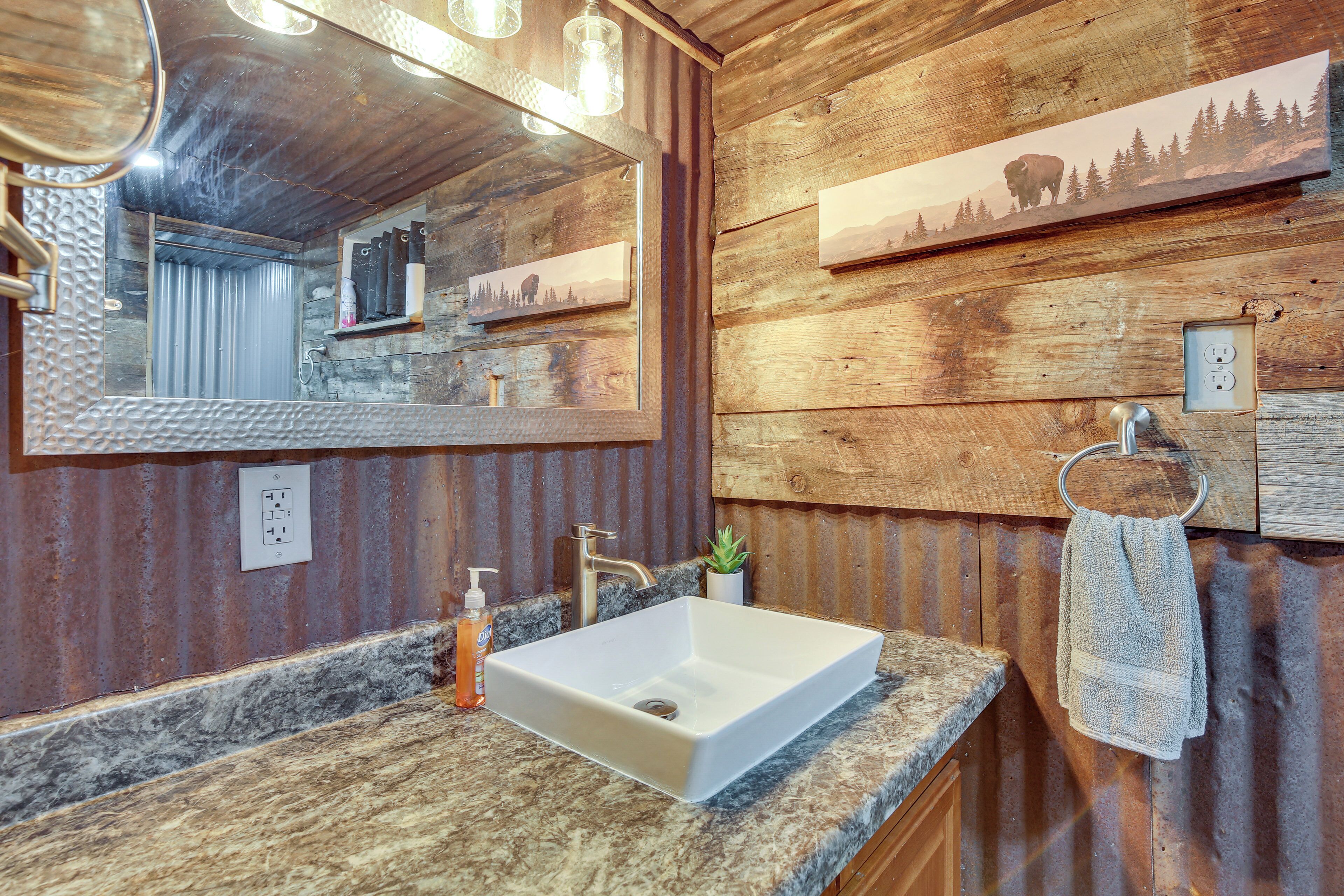 A rustic bathroom with a wooden wall, a large mirror, a white sink, and a towel rack.
