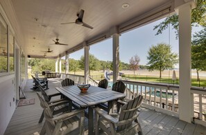 A covered outdoor area with a table and chairs, ceiling fans, and a view of a pool and trees.
