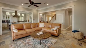 A spacious living room with a large L-shaped sectional sofa, a round coffee table, and a ceiling fan.