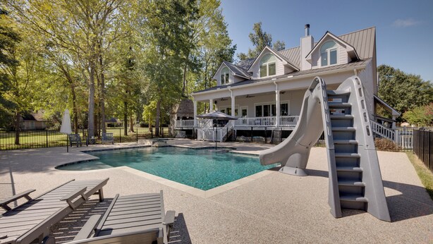 A swimming pool with a slide, lounge chairs, and a covered deck area.