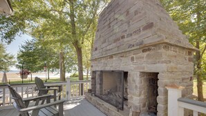 A stone fireplace on a wooden deck with Adirondack chairs.