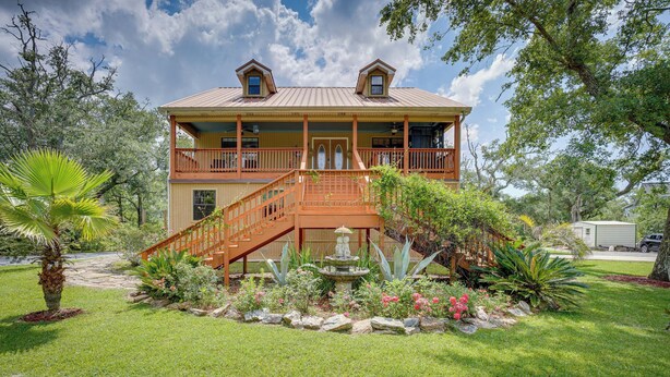 A two-story house with a balcony, a staircase leading to the second floor, and a small garden with a fountain. - Waterfront Pass Christian Oasis ~ 2 Mi to Beach! (Pass Christian)