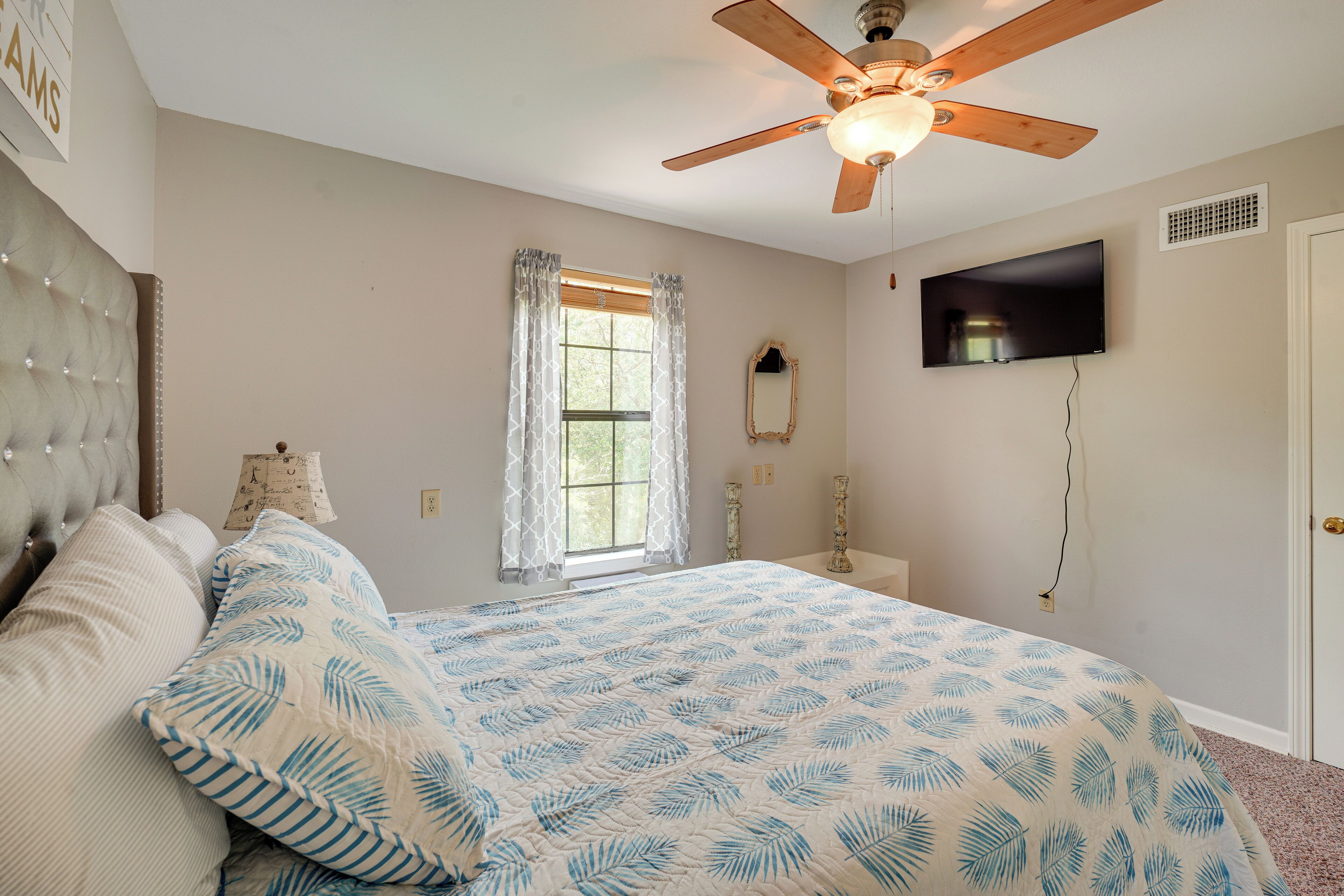 Une chambre à coucher comprenant un lit, un ventilateur de plafond, une fenêtre avec des rideaux, un téléviseur et un miroir.