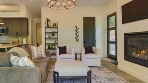 A living room with a sofa, chairs, a rug, a fireplace, and a kitchen area with cabinets and a microwave. - Modern Cabin w/ Hot Tub & Fire Pit in Fairview! (Fairview)